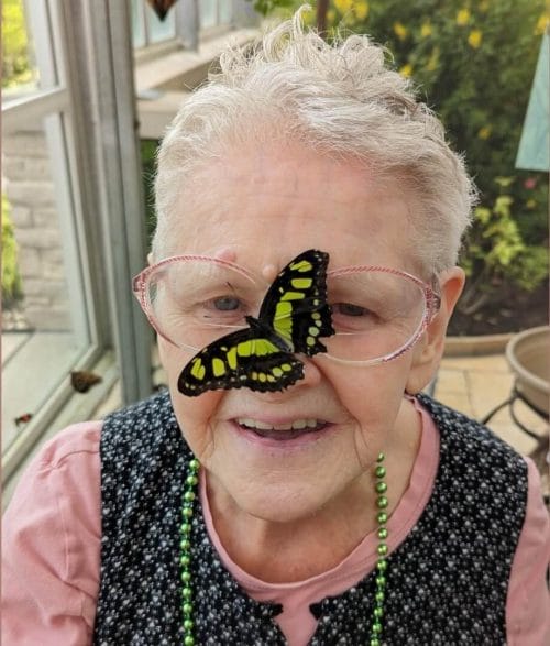 Opportunity House client smiling as a butterfly lands on their nose while visiting the Brookfield Zoo Butterfly Garden.