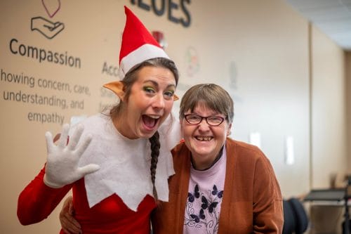 Smiling Opportunity House client with a staff member dressed as a Christmas elf during a holiday celebration.