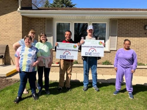 Opportunity House clients and staff standing in front of a home holding fundraising signs.