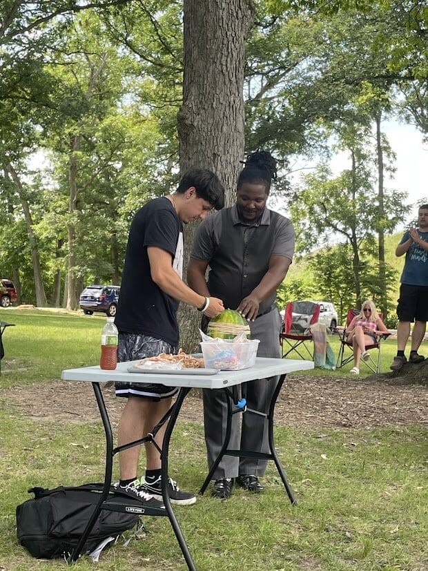 Two participants stretching rubber bands around a watermelon at Watermelon Explosion.