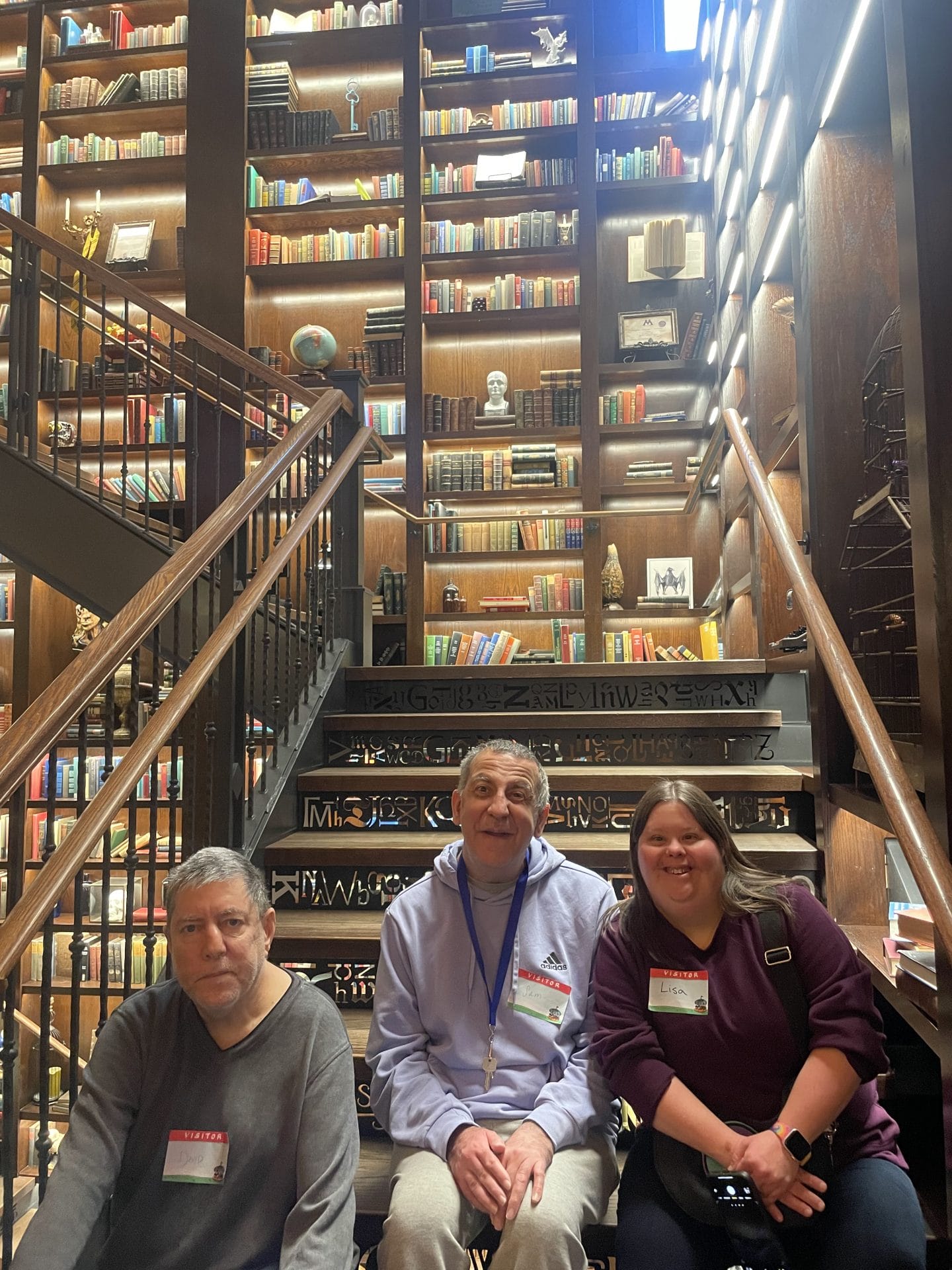 3 Opportunity clients sitting on stairs in front of a large bookshelf smiling for photo.