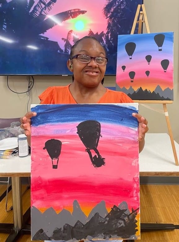 Opportunity House Recreation client smiling and posing with painting of hot air balloons.