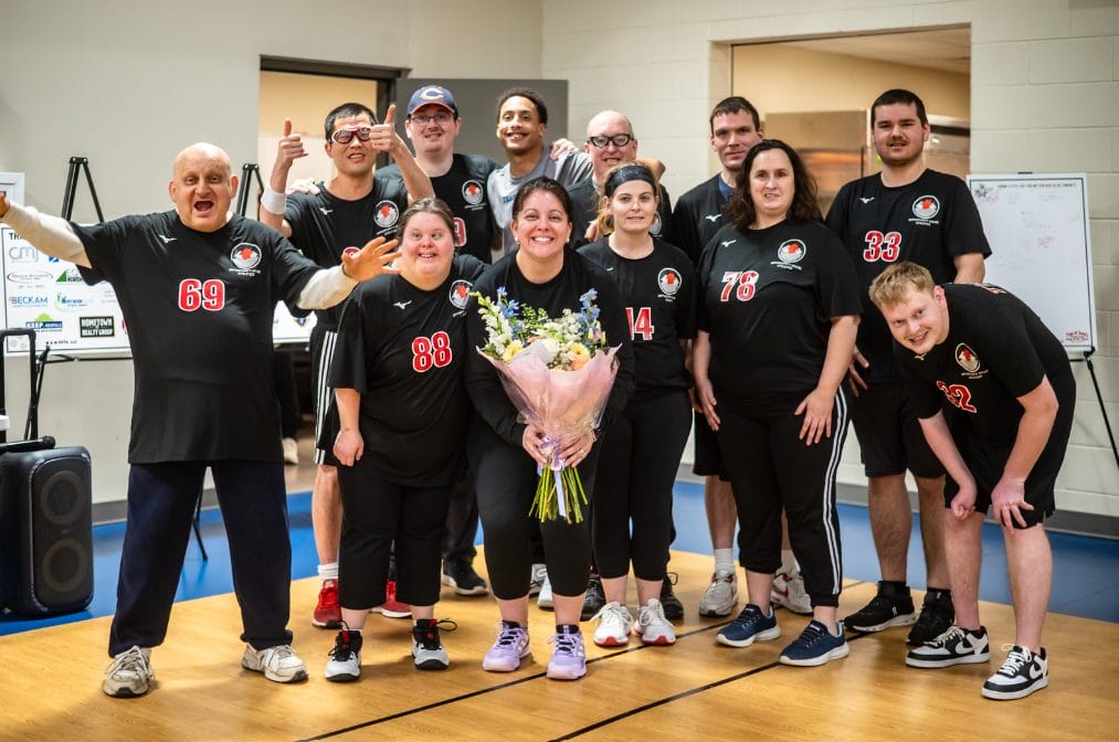 2026 Opportunity House Volleyball Event coordinator holding flowers alongside Opportunity House Athletics Volleyball Team posing for photo.