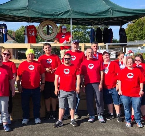 Group of Opportunity House Athletics Athletes wearing red OH Athletics shirts standing in front of Wheel of Meat Stage.